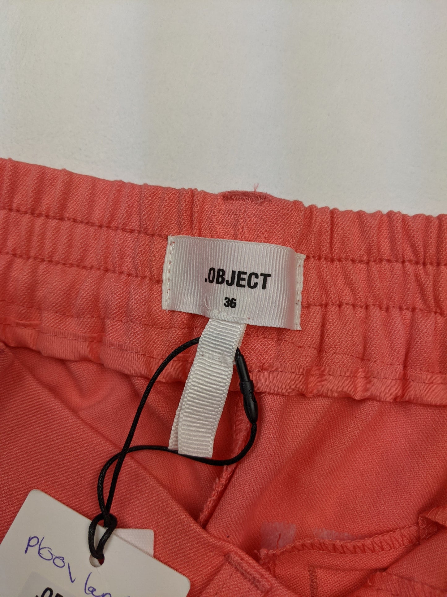 Close-up of OBJECT brand tag on coral trousers