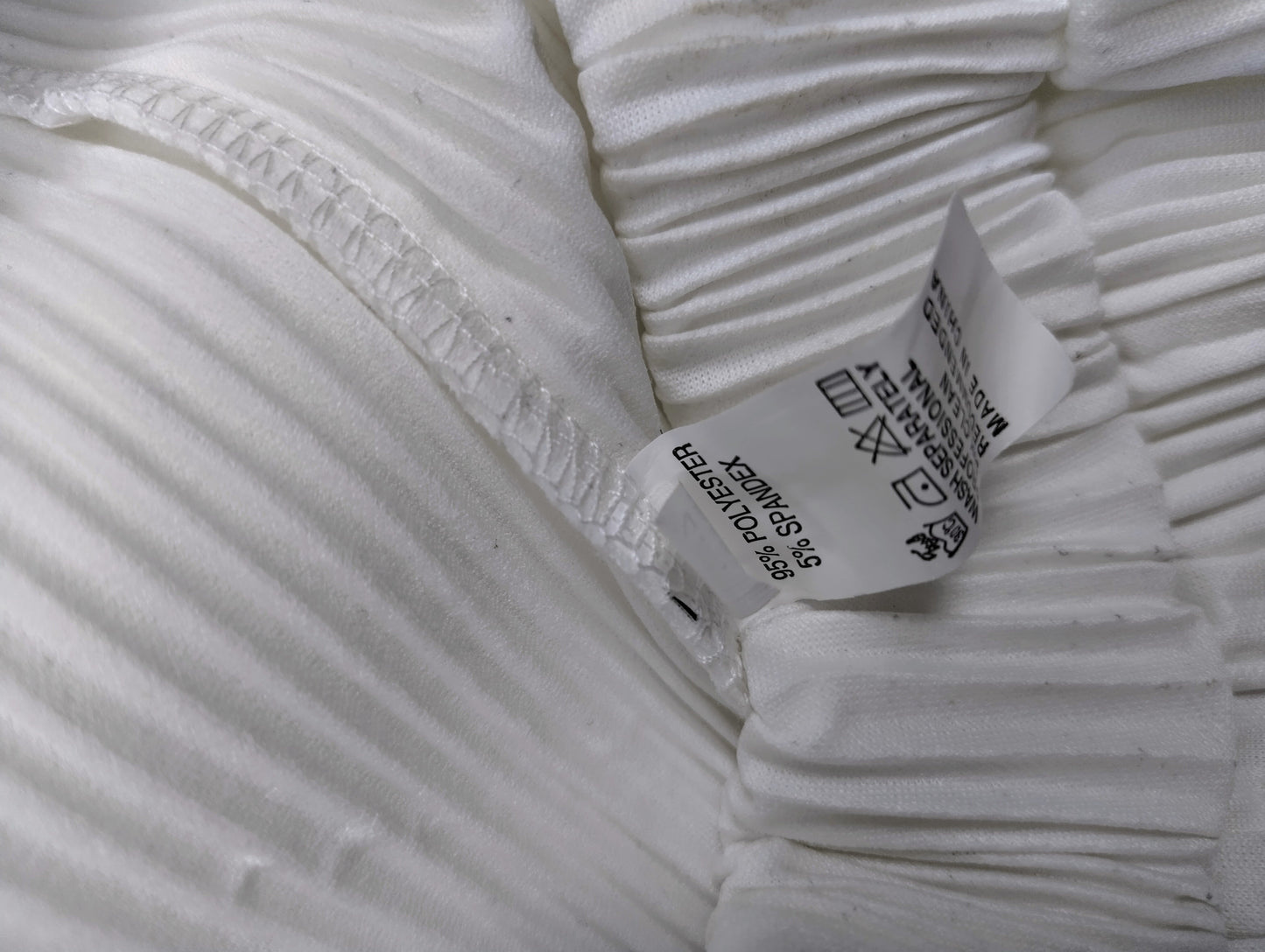Close-up of the inner label of the white pleated pants