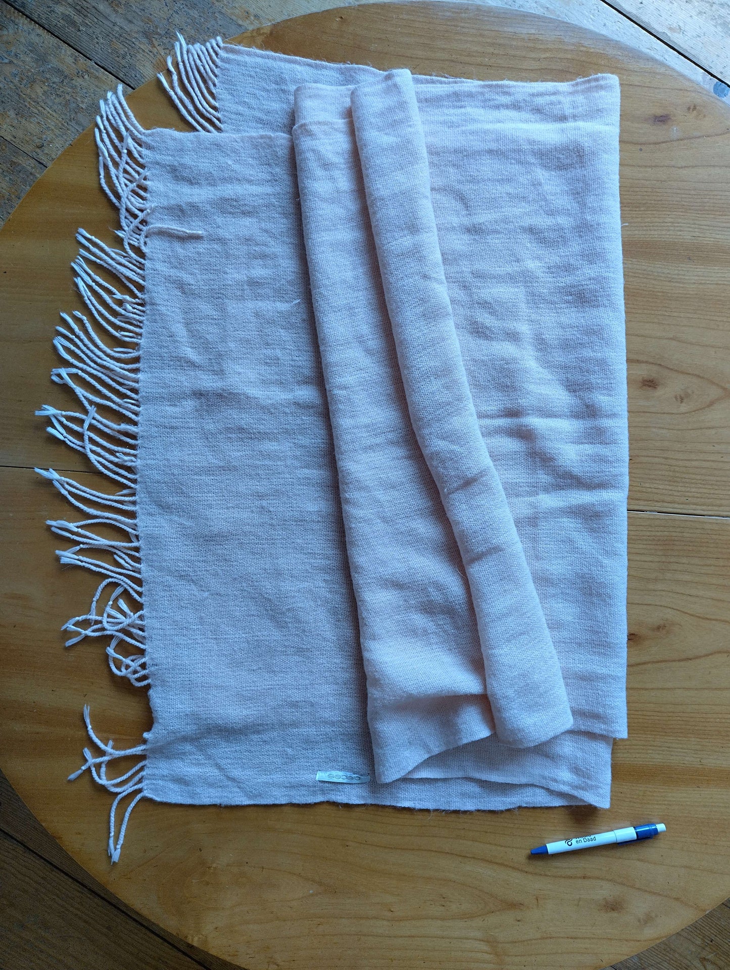 Folded pink scarf on a wooden table with pen for size reference