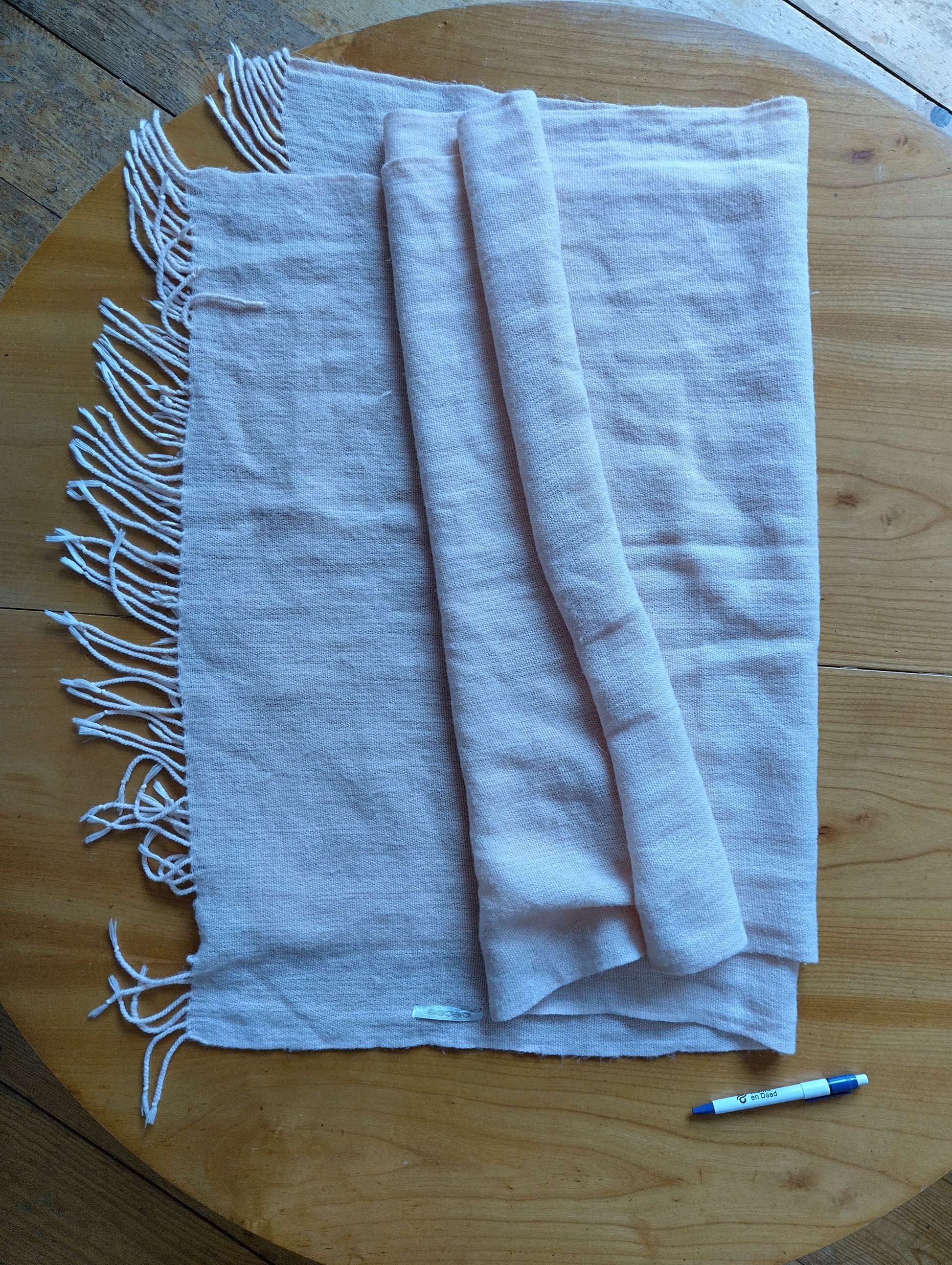 Folded pink scarf on a wooden table with pen for size reference