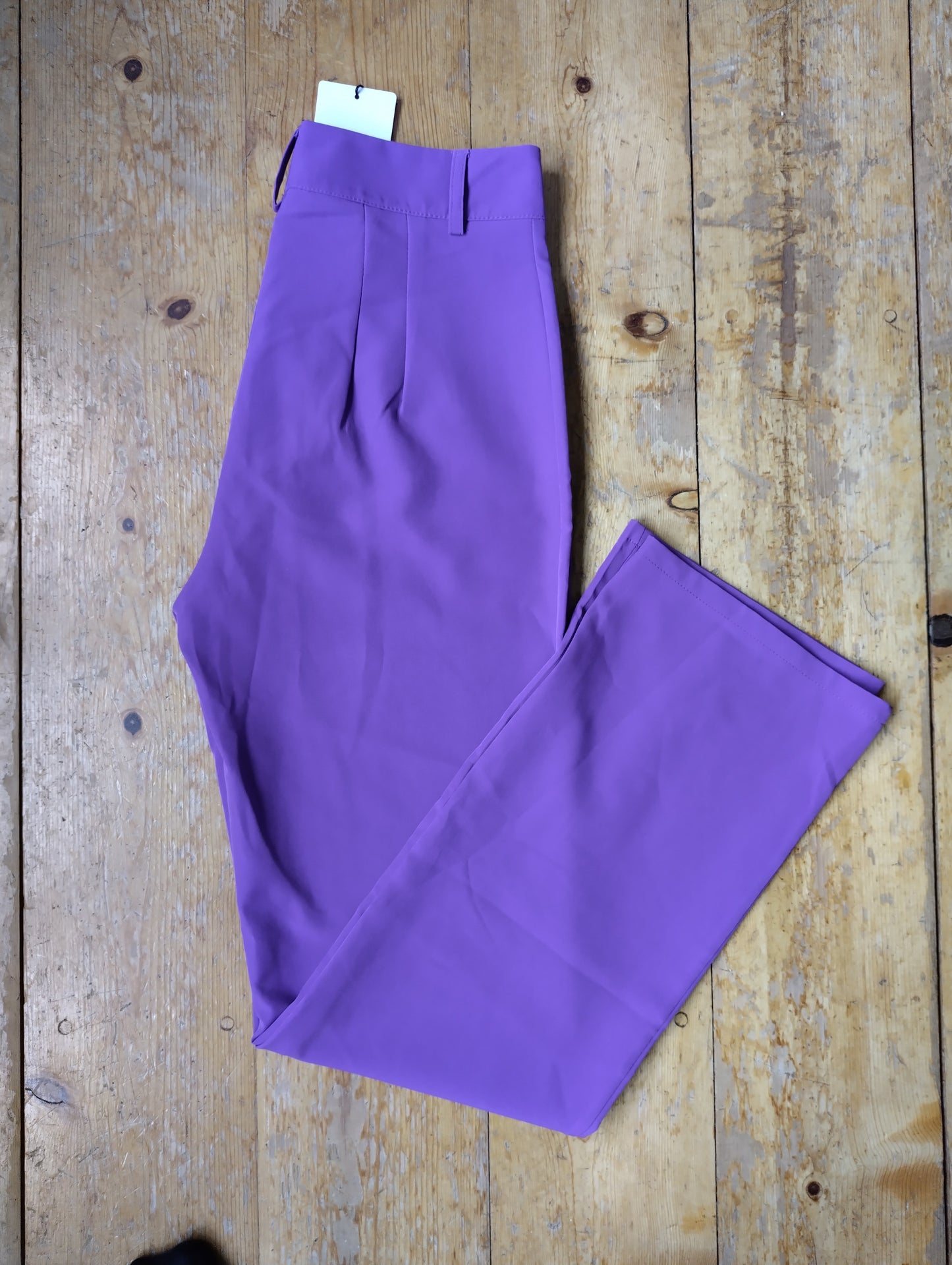 Purple wide-leg trousers folded on a wooden floor