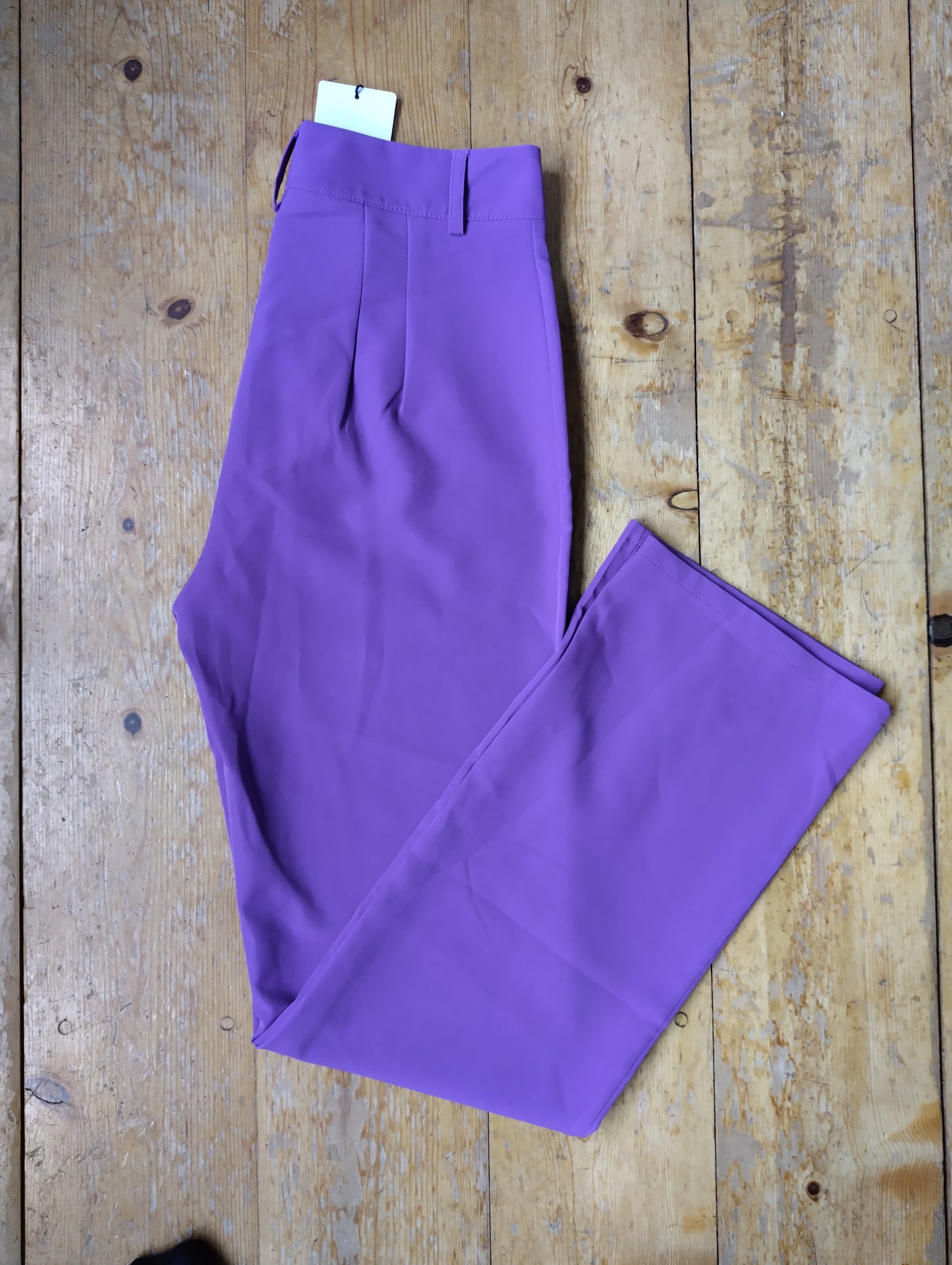 Purple wide-leg trousers folded on a wooden floor