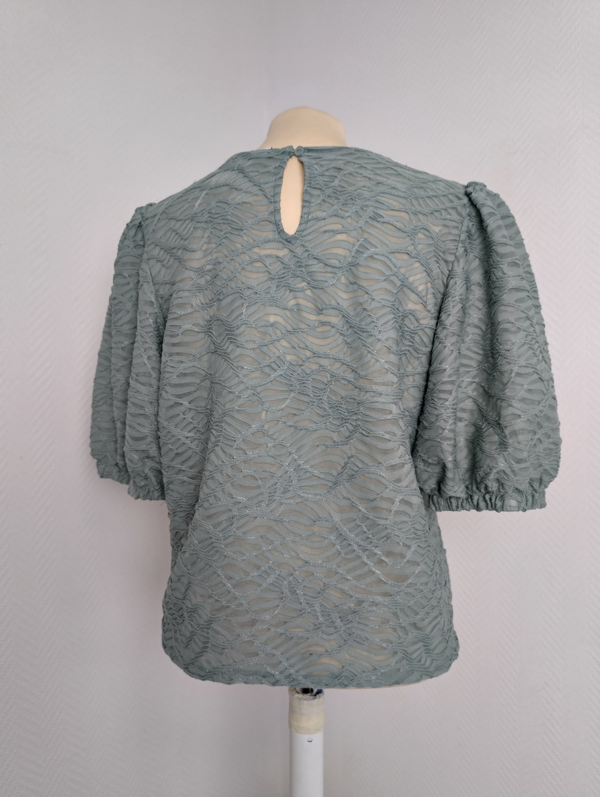 Back view of sage green lace blouse on mannequin