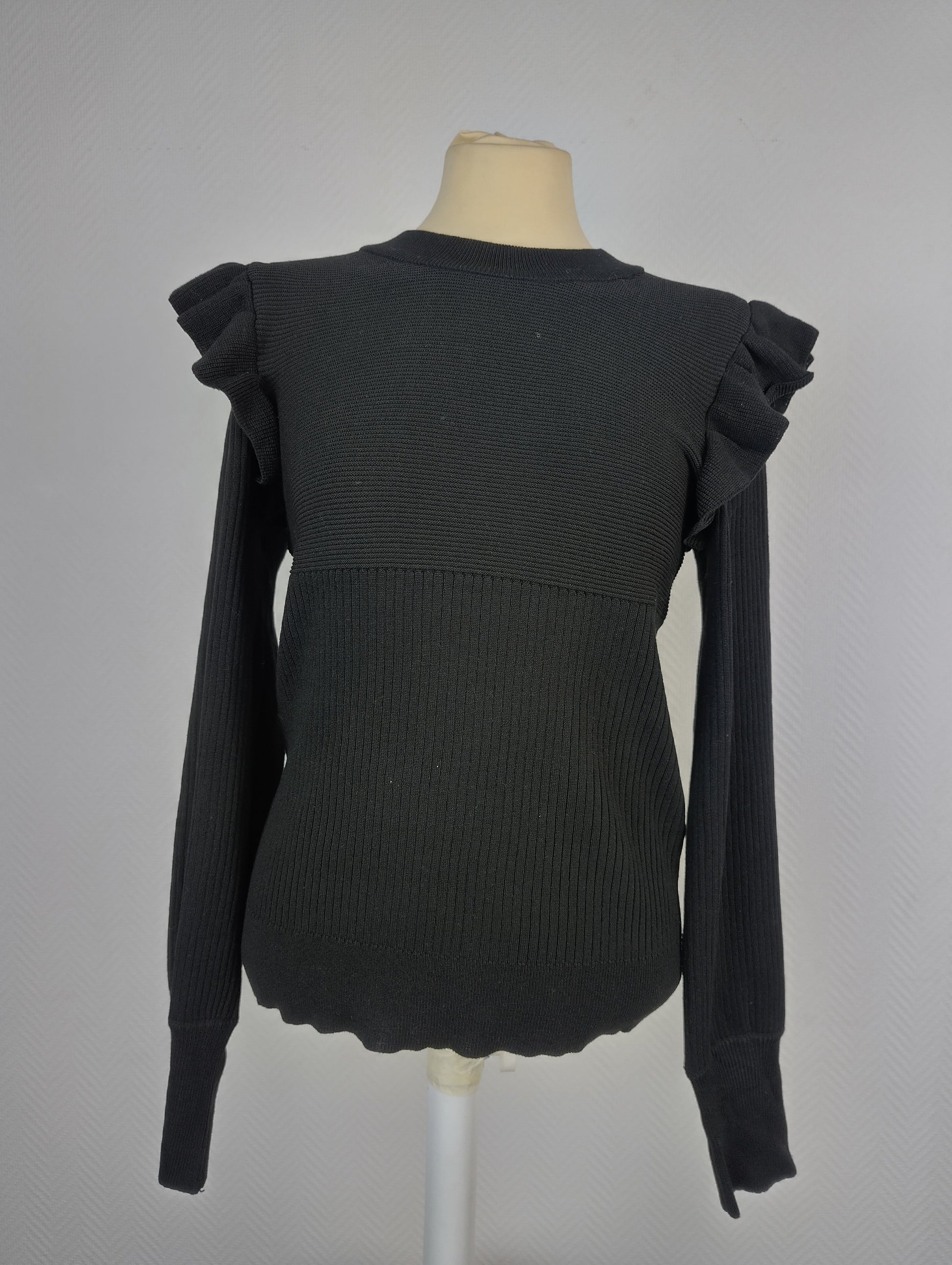 Front view of black ribbed knit top with ruffle shoulders
