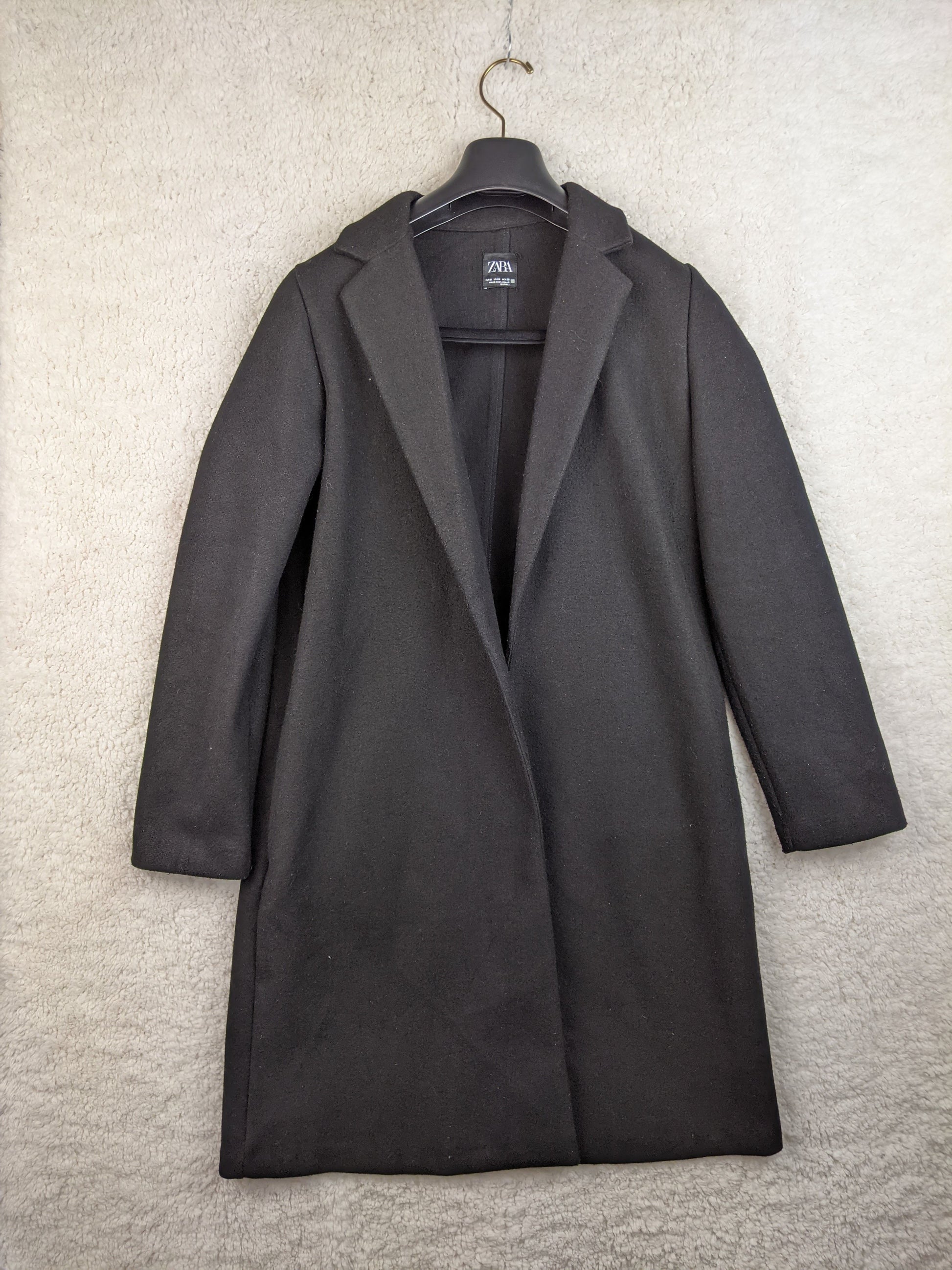 Front view of black coat hanging on a hanger