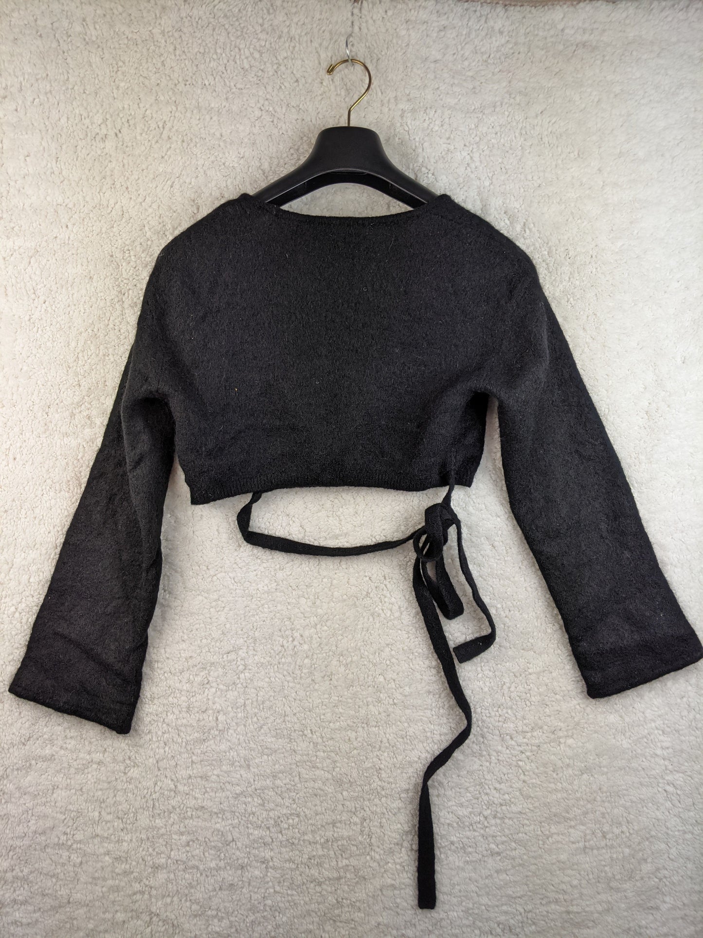 Back view of black wrap cropped sweater on hanger